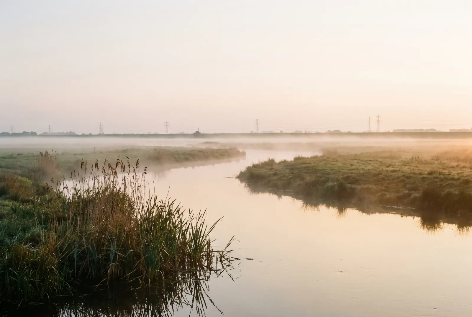 A river bending through a misty meadow with distant pylons